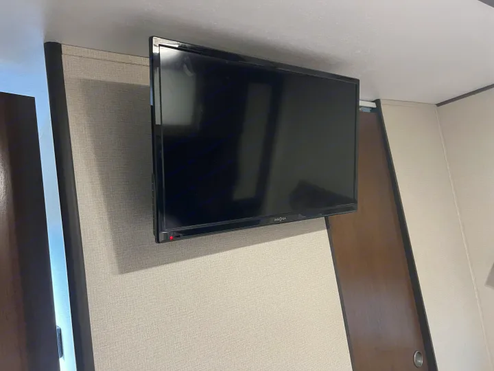 An Insignia flat-screen TV is mounted on a light, textured wall inside an RV rental, showing a red power indicator light.. Avenger 31DBS 2019