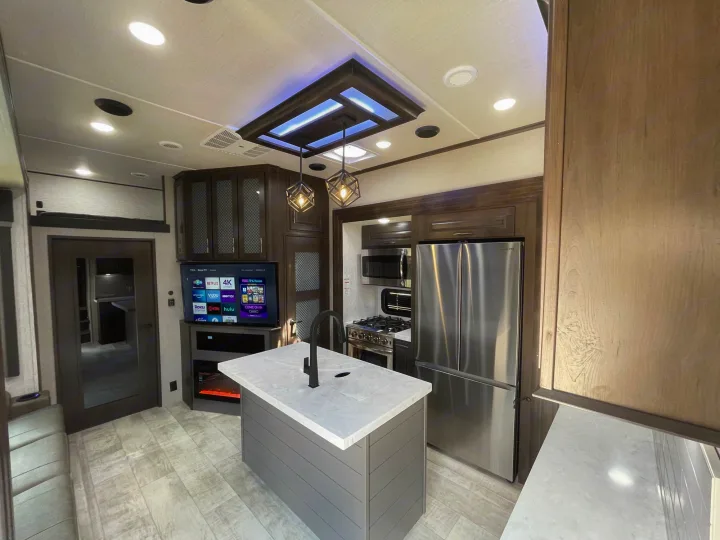Spacious modern RV rental kitchen & living area with island, appliances, and TV, featuring light flooring and dark wood accents.. Momentum Grand Design M-351 2023