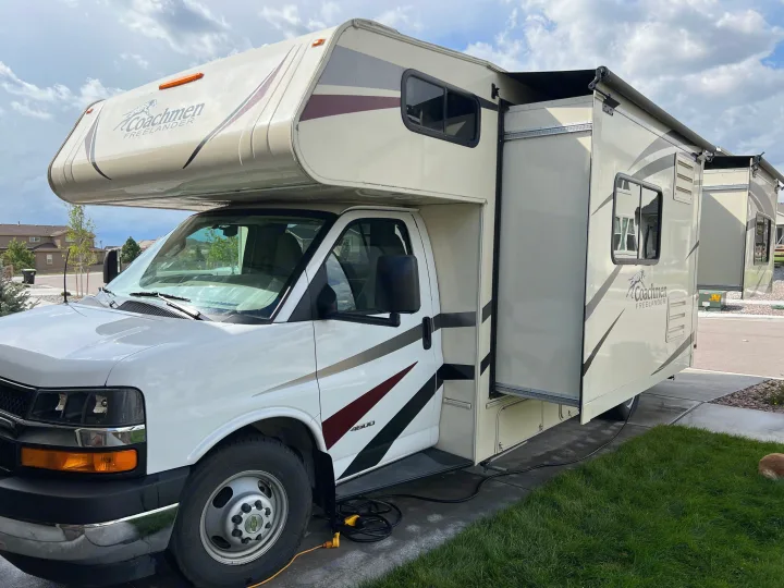 White Coachmen Freelander RV rental with extended slide-out and power cords, parked on pavement next to grass.. Forest River Coachmen Freelander 2019