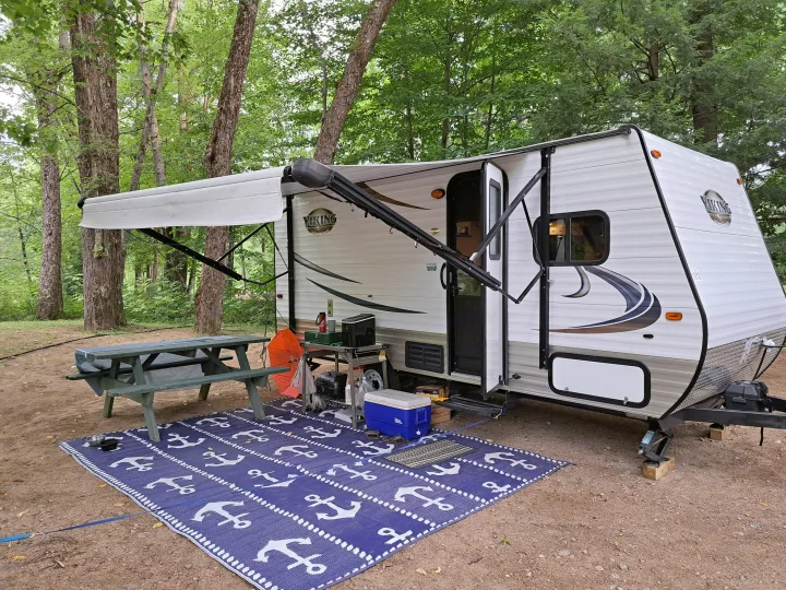 Spacious RV rental setup at a peaceful campsite with an extended awning, picnic table, and outdoor mat.. Forest River Viking Saga 2016