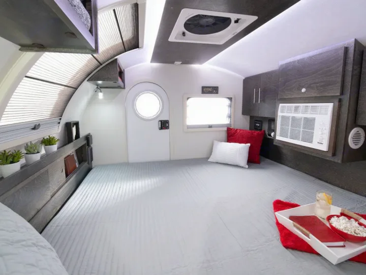 Cozy RV rental interior with a large bed, built-in storage, and AC for comfortable compact living. Perfect for adventure!. nuCamp T@G XL Boondock 2022