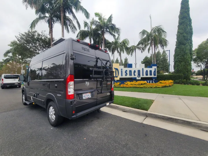 Dark gray RV rental (Ram ProMaster van) parked curbside at the Disneyland Hotel. Features bike rack & rooftop solar panels.. Thor Motor Coach Rize 18M 2023