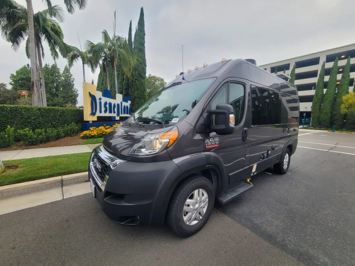 Dark gray Ram ProMaster RV rental van parked near the Disneyland sign, surrounded by palm trees and green landscaping.. Thor Motor Coach Rize 18M 2023