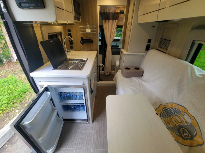 RV rental interior showcasing a kitchen with stove & open fridge, cozy seating, and a table. Ready for travel.. Thor Motor Coach Rize 18M 2023