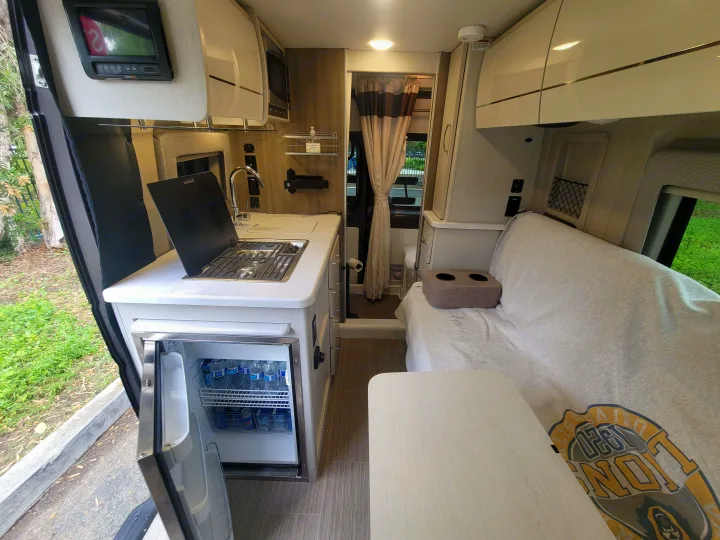 This rv rental offers a compact, functional interior. It features a kitchenette with stove, sink, and fridge, plus a sofa and table.. Thor Motor Coach Rize 18M 2023
