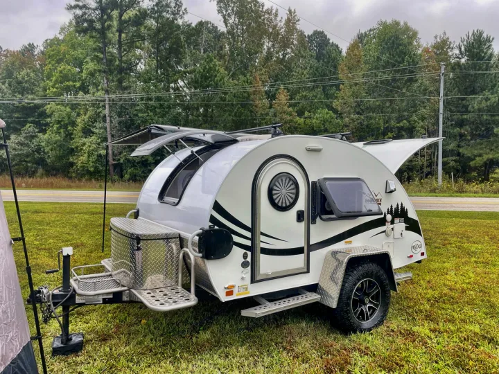 A modern white & black teardrop RV rental, with hatches open, ready for camping on green grass.. nuCamp T@G 2021