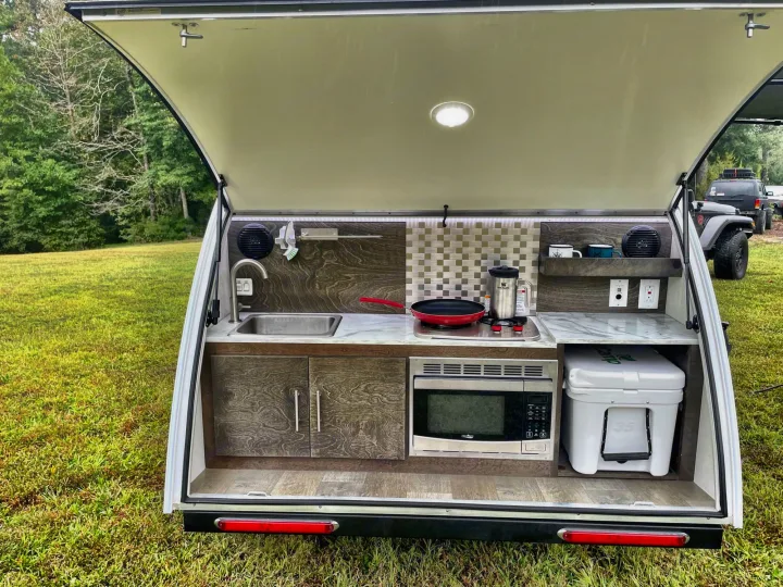 Experience outdoor cooking with this RV rental teardrop camper kitchen: sink, microwave, stove, & YETI cooler.. nuCamp T@G 2021
