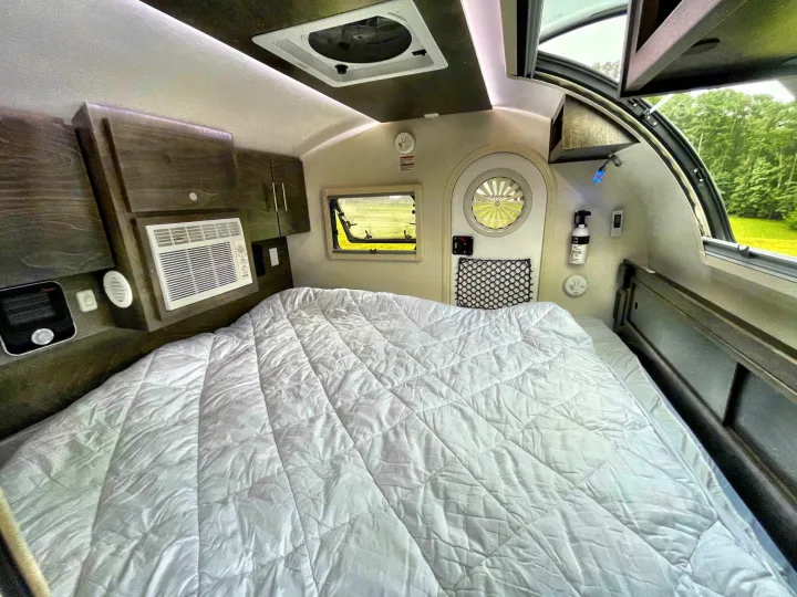 Bright, compact rv rental interior featuring a large bed, AC unit, and scenic windows for comfortable travels.. nuCamp T@G 2021