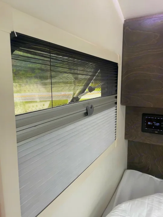 RV rental: A window with an integrated mesh screen and pleated privacy blind. Digital clock shows 5:30 AM.. nuCamp T@G 2021