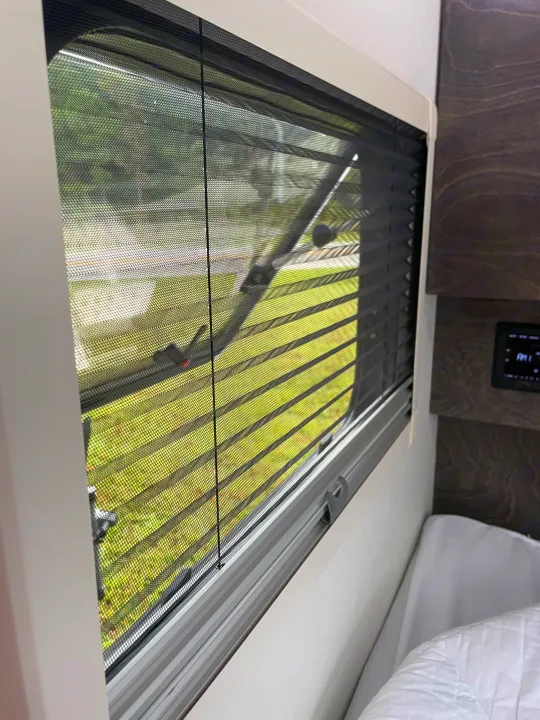 An RV rental's multi-functional window with insect screen & privacy blind, overlooking green nature.. nuCamp T@G 2021