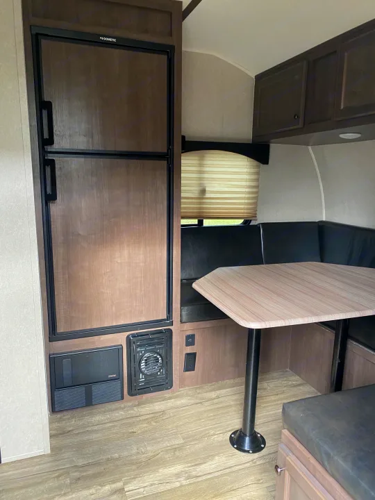 RV rental interior featuring a Dometic fridge, dinette with table and L-shaped seating, cabinets, and a window.. Sunset Park RV Sun Lite 2020
