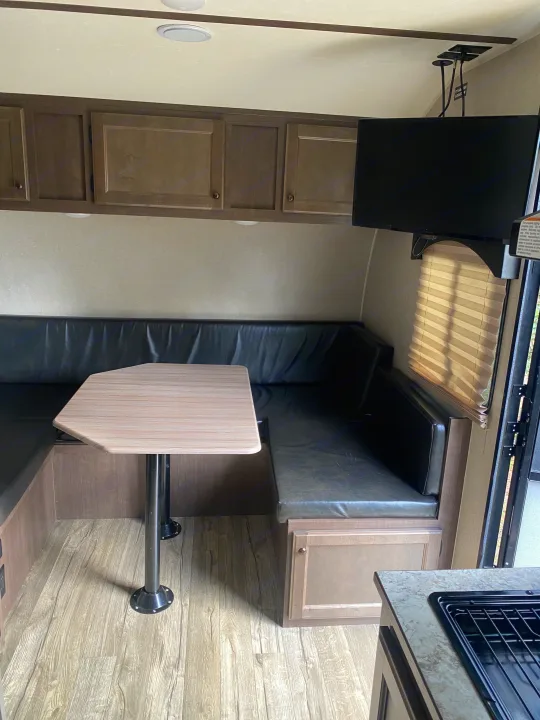 RV rental interior featuring a comfortable dinette with U-shaped seating, table, cabinets, and mounted TV.. Sunset Park RV Sun Lite 2020