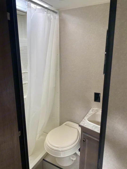 Compact RV rental bathroom with shower, toilet, and sink vanity. Functional layout for travelers.. Sunset Park RV Sun Lite 2020