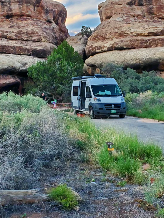 White RV rental at campsite 10, nestled between towering rock formations and green shrubbery. Great for outdoor adventures.. Custom Camper 2017