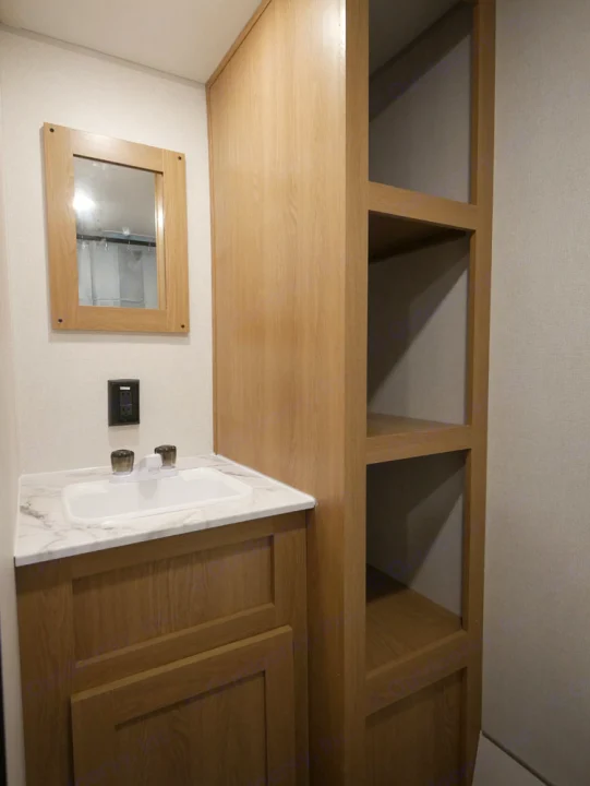 This RV rental bathroom features a light wood vanity with a sink, mirror, and practical open storage shelving.. Forest River Avenger 2022