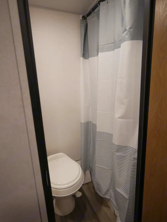 RV rental's compact bathroom with a white toilet and a stylish striped shower curtain.. Forest River Avenger 2022
