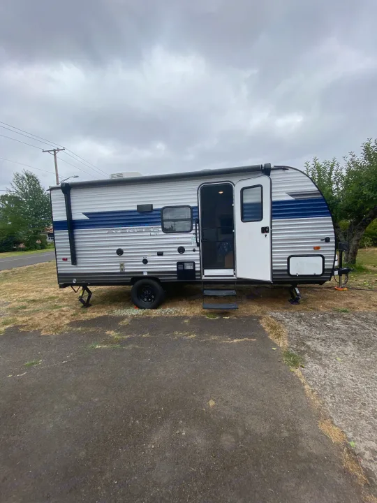 This RV rental travel trailer is parked with its door open and stabilizer jacks down, ready for camping.. Forest River Avenger 2022