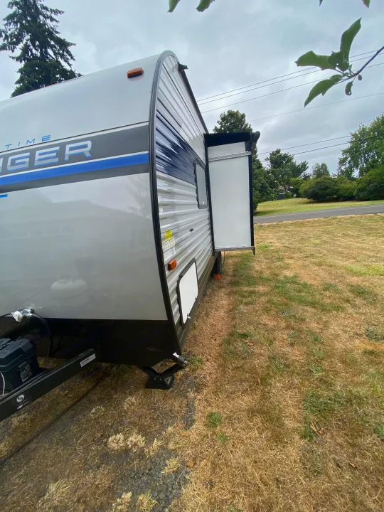 RV rental: Gray travel trailer with extended slide-out, parked on dry grass under an overcast sky.. Forest River Avenger 2022