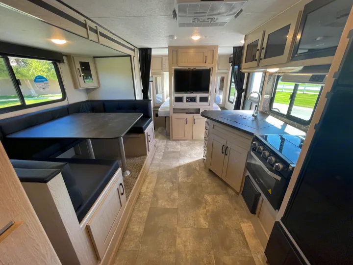 RV rental interior: modern light wood, black dinette, kitchen, entertainment area, and peek into the rear bedroom.. Coachmen Apex 2022