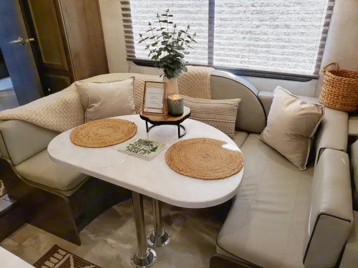 Cozy RV rental dinette with a marble-look table, comfortable bench seating, decorative pillows, and a window.. Gulf Stream Conquest 2022