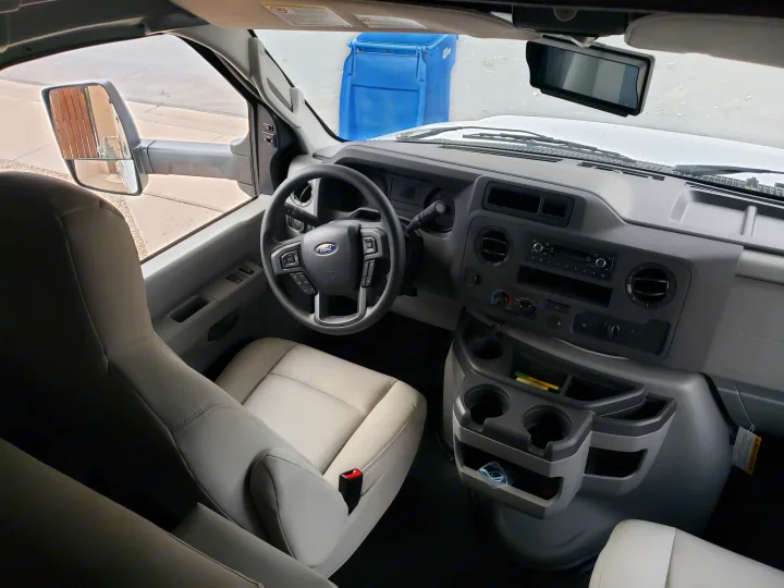 Interior view of an RV rental, showcasing the Ford steering wheel, dashboard controls, and light-colored front seats.. Gulf Stream Conquest 2022