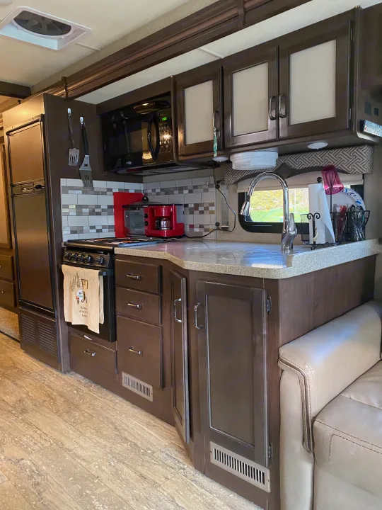 RV rental kitchen interior: dark cabinets, full oven, microwave, fridge, and sink. Ready for mobile cooking and travel adventures.. Thor Hurricane 2018