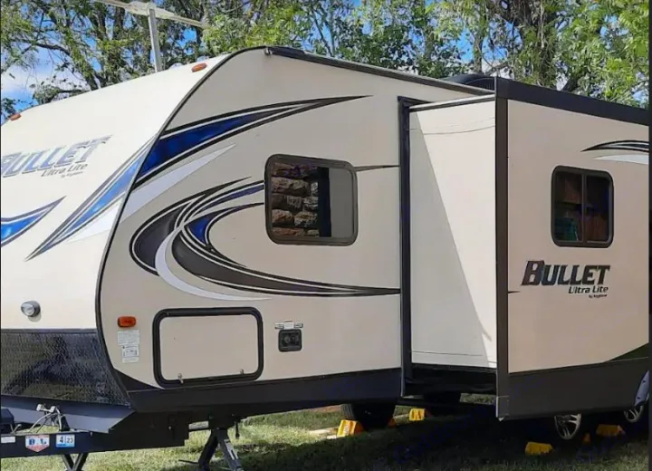A beige Bullet Ultra Lite travel trailer, an RV rental, is shown parked outdoors with its side slide extended.. Keystone RV Bullet Ultra Lite 2016