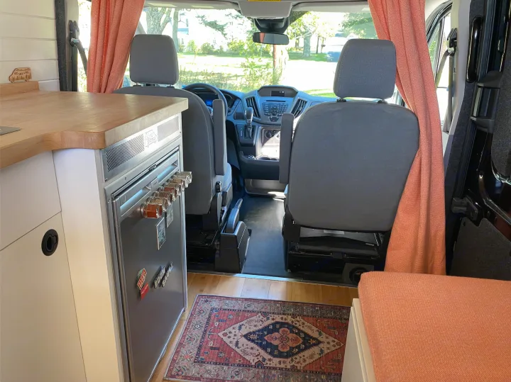 Cozy rv rental interior: custom camper van kitchen with fridge & spices, wooden floor, and front cabin view. Ready for adventure.. Ford Transit 2019