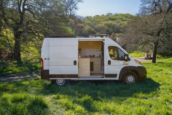 Ready for adventure! White **rv rental** campervan with open kitchen, parked in a vibrant green field.. ram ProMaster 2021