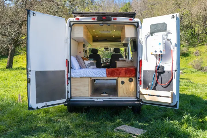 RV rental: Custom campervan's rear doors open, revealing a built-in bed, storage, and exterior shower.. ram ProMaster 2021