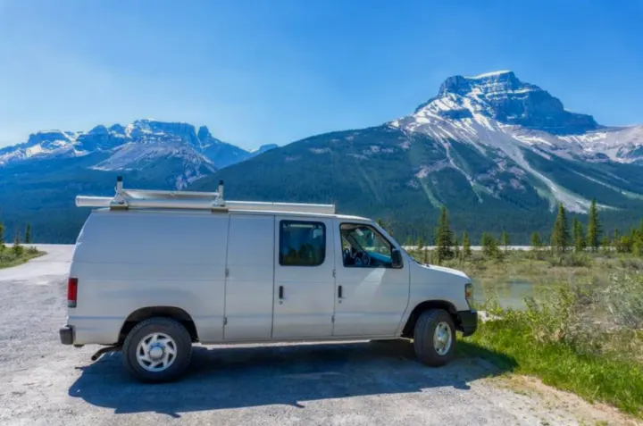 White RV rental van by a lake in mountains. Ideal for scenic nature adventures among snow-capped peaks & forests.. Ford Econolline 250s 2008