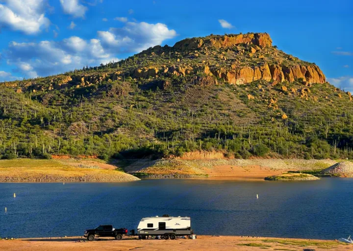 Enjoy an RV rental adventure! A black truck and travel trailer are parked by a scenic desert lake with saguaro-filled mountains.. Jayco Featherlight SLX8 2022