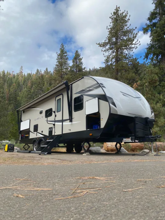 An RV rental travel trailer set up at a forest campsite with an awning extended and a generator ready.. Starcraft Super Lite 2022