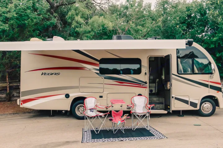 Beige Thor Vegas RV rental with extended awning, camping chairs, and a mat on the ground, ready for outdoor leisure.. Thor Vegas 2018