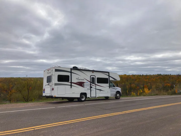 White RV rental parked on a road shoulder, overlooking autumn trees under a cloudy sky. Ideal for fall road trips.. Coachman Freelander 27QB 2011