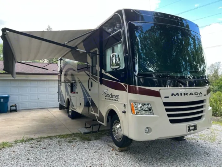 A cream and black Coachmen Mirada Class A motorhome with awning extended, parked in a driveway. Ideal for rv rental adventures.. Coachman Mirada 2018