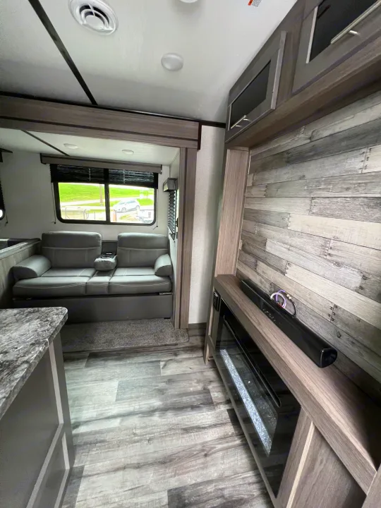 RV rental interior: modern gray sofa, wood-look flooring, and an entertainment center with fireplace.. Crossroads RV Volante 2022