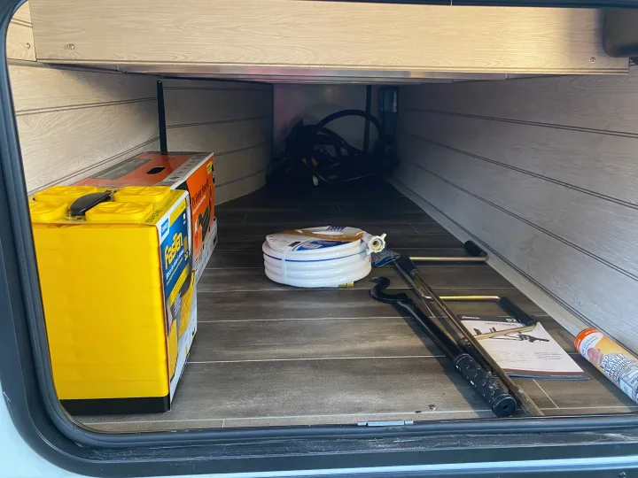 RV rental storage organized with essential gear: leveling blocks, fresh water hose, sewer kit, and hitch tools.. Keystone Passport 2022