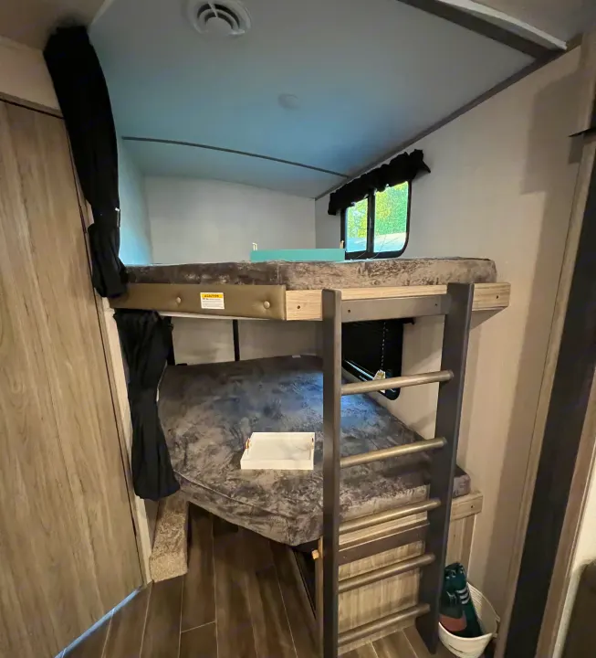 Cozy bunk beds in an RV rental, complete with dark grey bedding, a ladder, and a window view.. Keystone Passport 2022