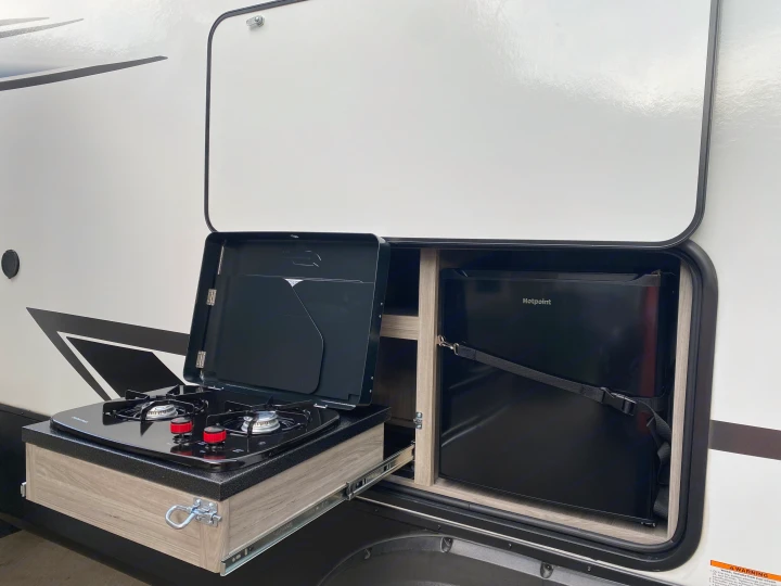RV rental featuring a compact outdoor kitchen with a pull-out two-burner stove and Hotpoint mini-fridge for camping.. Keystone Passport 2022