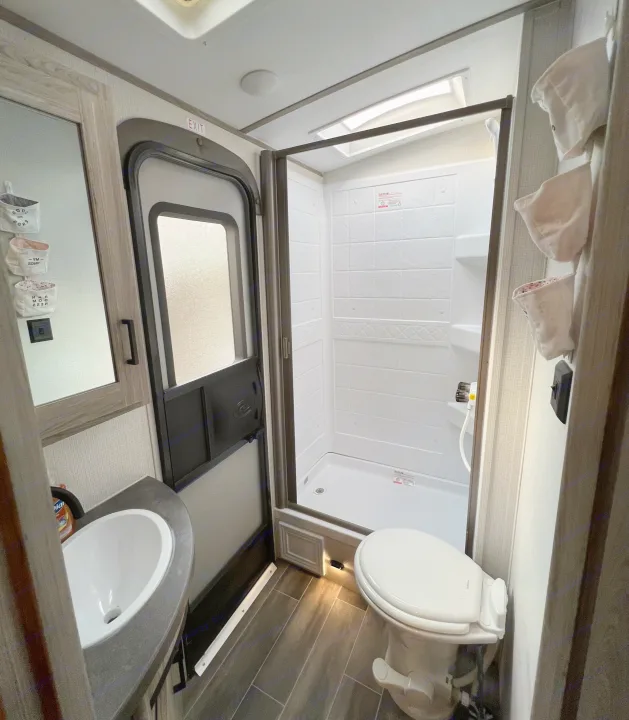 Compact RV rental bathroom featuring a pristine shower, toilet, and vanity with sink and mirror.. Keystone Passport 2022