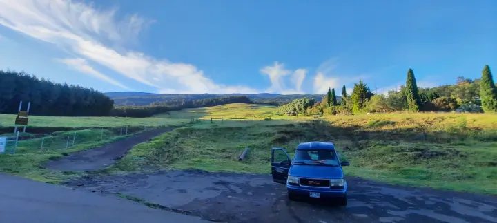 Blue GMC van parked in a scenic rural setting with rolling green hills and forests. Your RV rental adventure awaits!. Gmc Safari AstroVan 2000