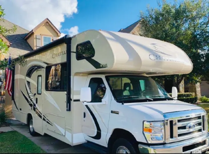 White and tan Class C motorhome, perfect for an rv rental road trip, parked in a sunny residential driveway.. Thor Chateau 2019