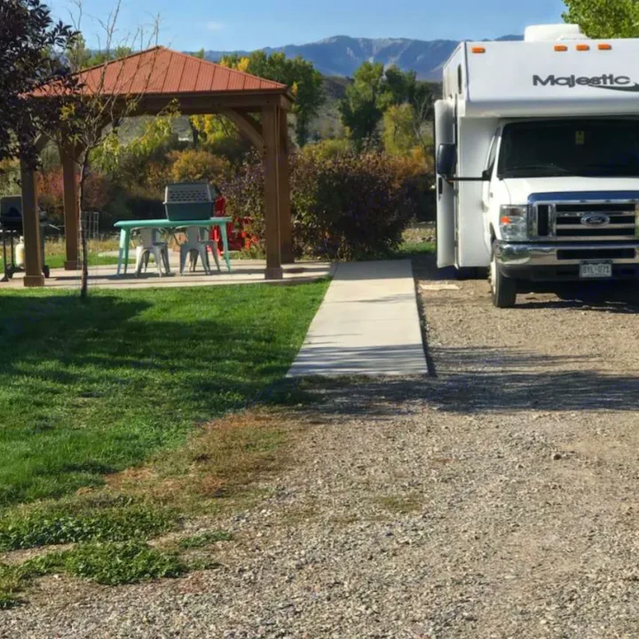 RV rental parked on gravel. A concrete path leads to a shaded gazebo with a table and chairs at a scenic site.. Thor Majestic 2017