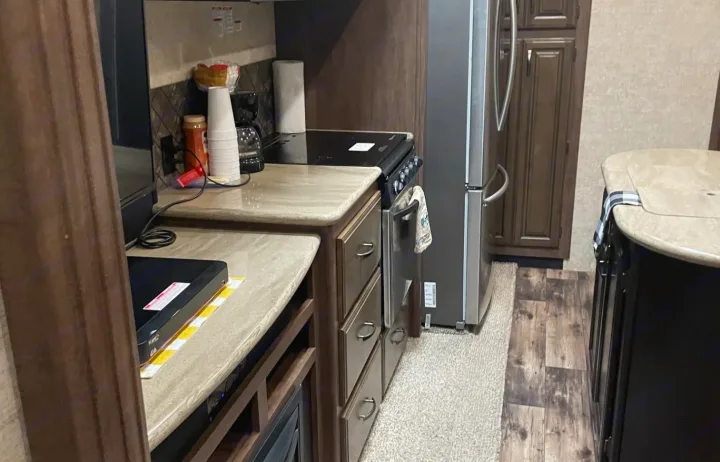 RV rental kitchen: compact yet functional space with fridge, stove, and ample counter. Ideal for travel cooking.. Forest River Sandpiper 2018