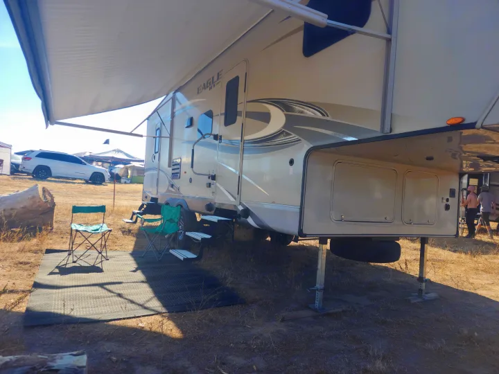 Spacious Jayco fifth-wheel RV rental at a dry outdoor campsite, with extended awning, chairs, and mat.. Jayco Eagle HT 2018