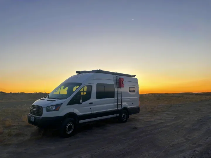 White camper van, potentially an RV rental, parked in a field at sunset with a crescent moon. Perfect for outdoor adventures!. Ford Transit Custom 2019