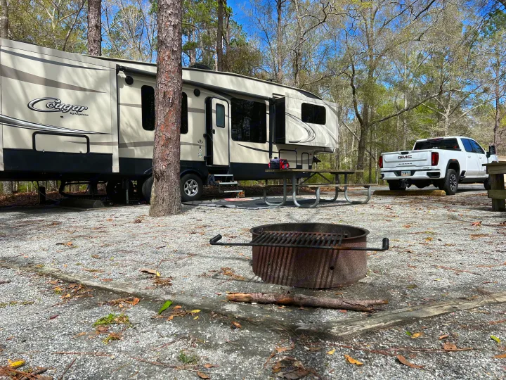 Spacious Cougar RV rental and GMC truck at a gravel campsite. Features a picnic table and fire pit, ideal for outdoor adventures.. Keystone RV Cougar 2017