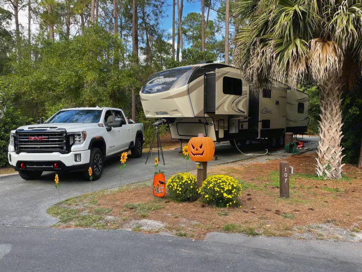 A white truck and a large fifth-wheel RV (Cougar) are parked on a paved campsite decorated for fall. Ideal for an RV rental experience.. Keystone RV Cougar 2017