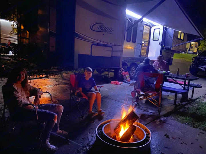 Evening at an **rv rental** campsite: Family enjoys a crackling bonfire, surrounded by large RVs, for a relaxing outdoor experience.. Keystone RV Cougar 2017